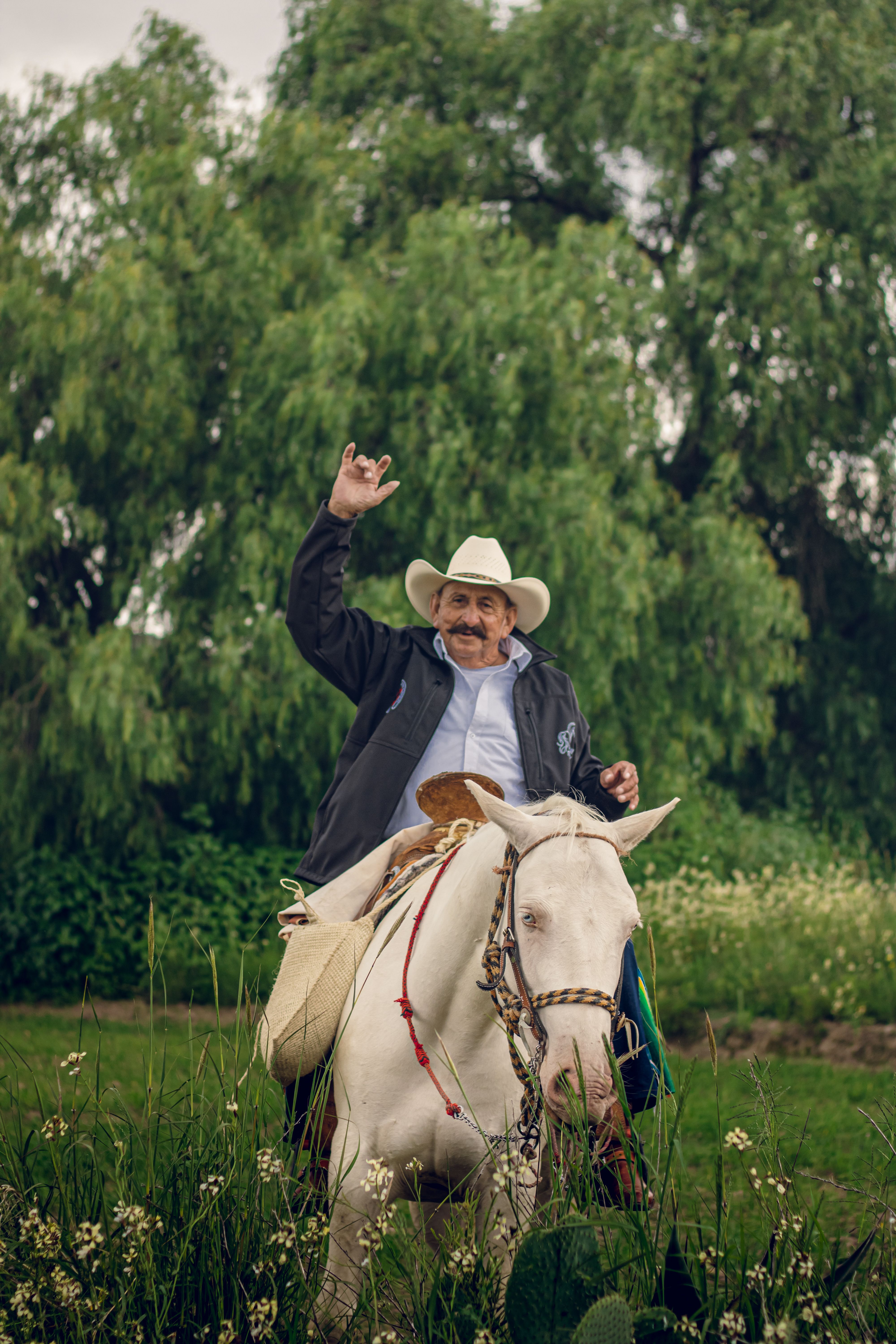 A cheerful cowboy waves from his horse in a scenic landscape in Pachuca, Mexico.