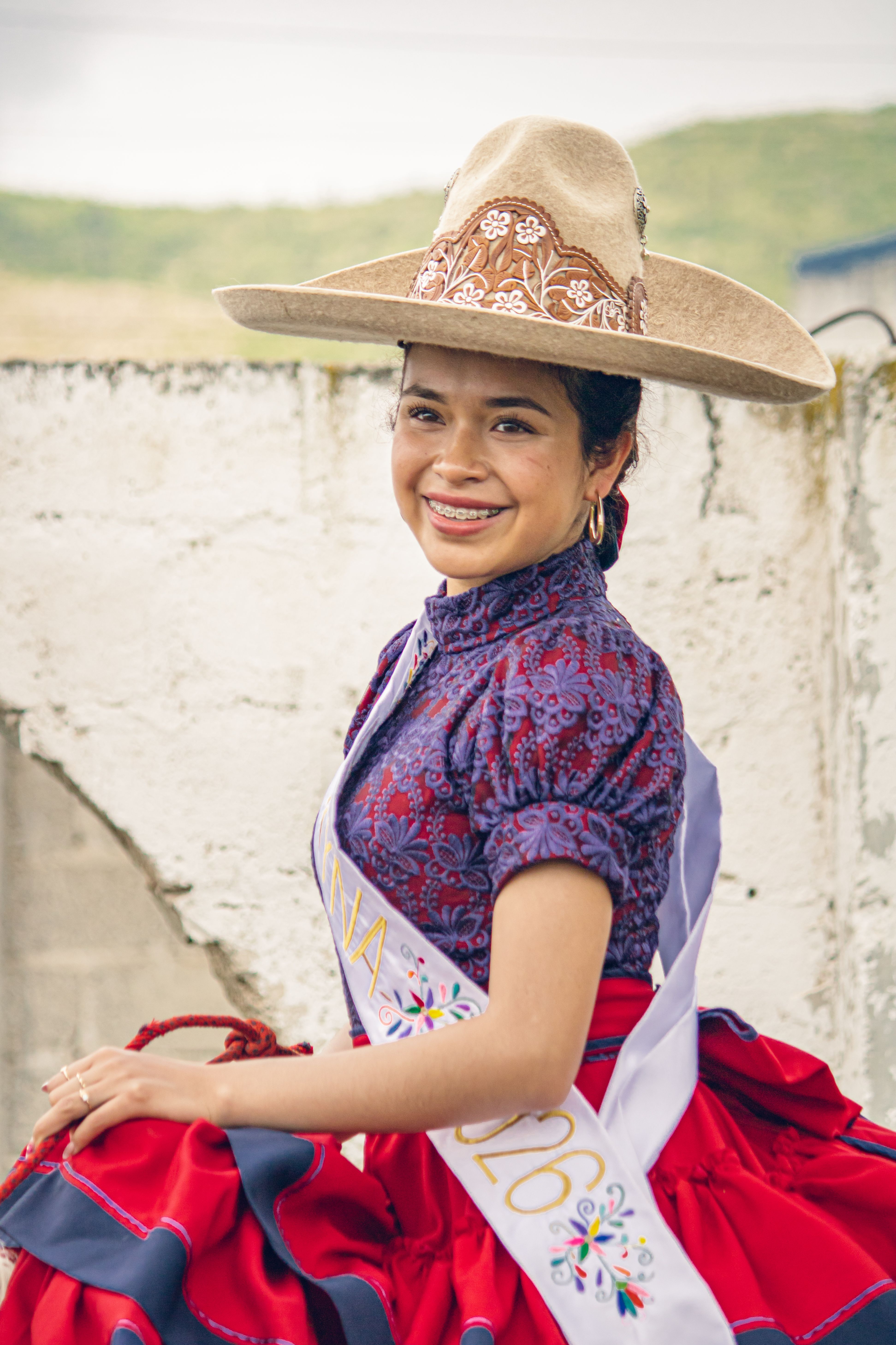 Portrait of a smiling young woman in traditional Mexican charro attire with a decorative hat, representing cultural heritage.
