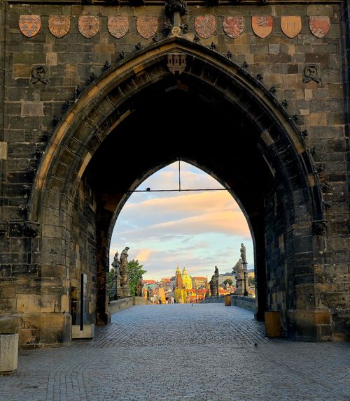 Free View of Prague through a Gothic archway leading to Charles Bridge at sunset. Stock Photo