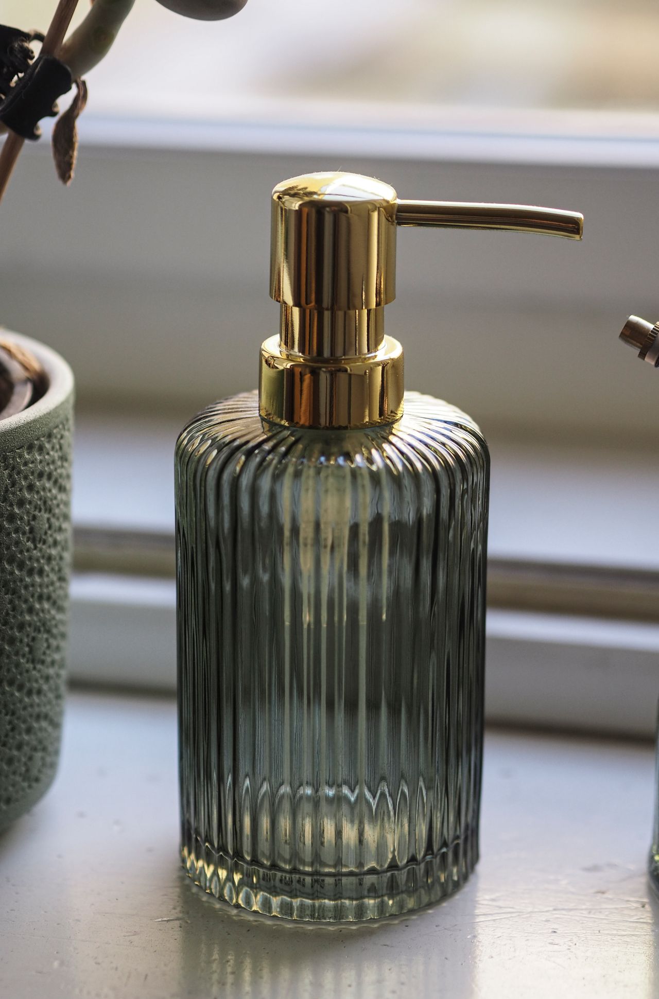 Ribbed glass soap dispenser with a gold pump on a windowsill