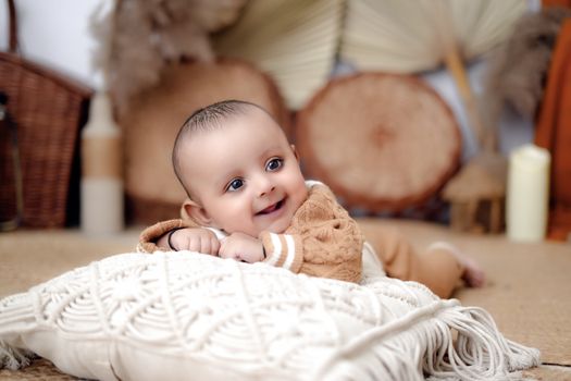 Charming baby lying on a textured cushion, smiling warmly in a cozy indoor setting.