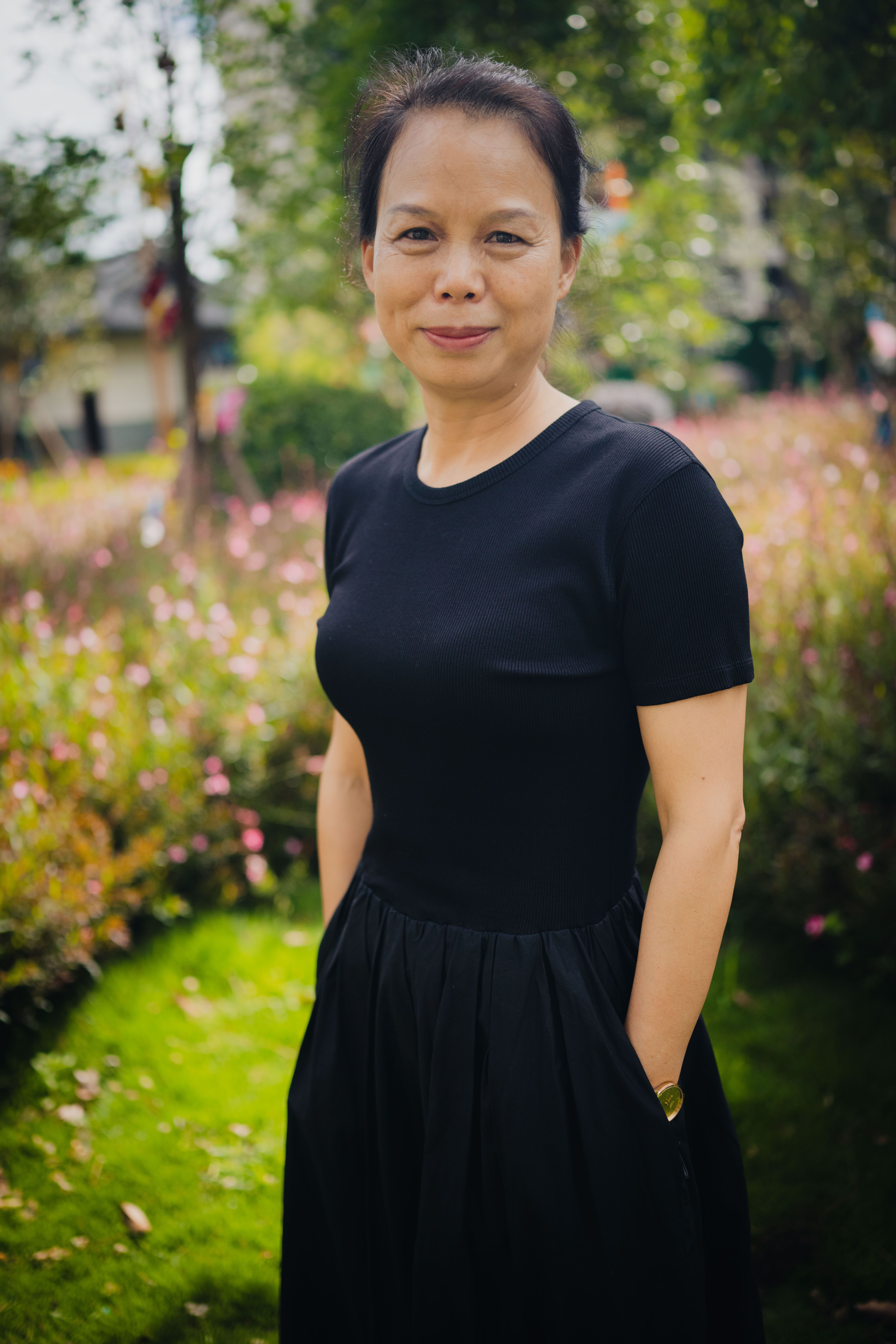 Smiling woman in a black dress standing in a lush garden with flowers.