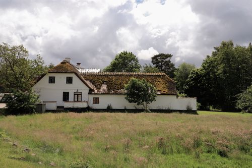 Free Charming traditional Danish farmhouse in a lush green rural landscape with a dramatic sky. Stock Photo