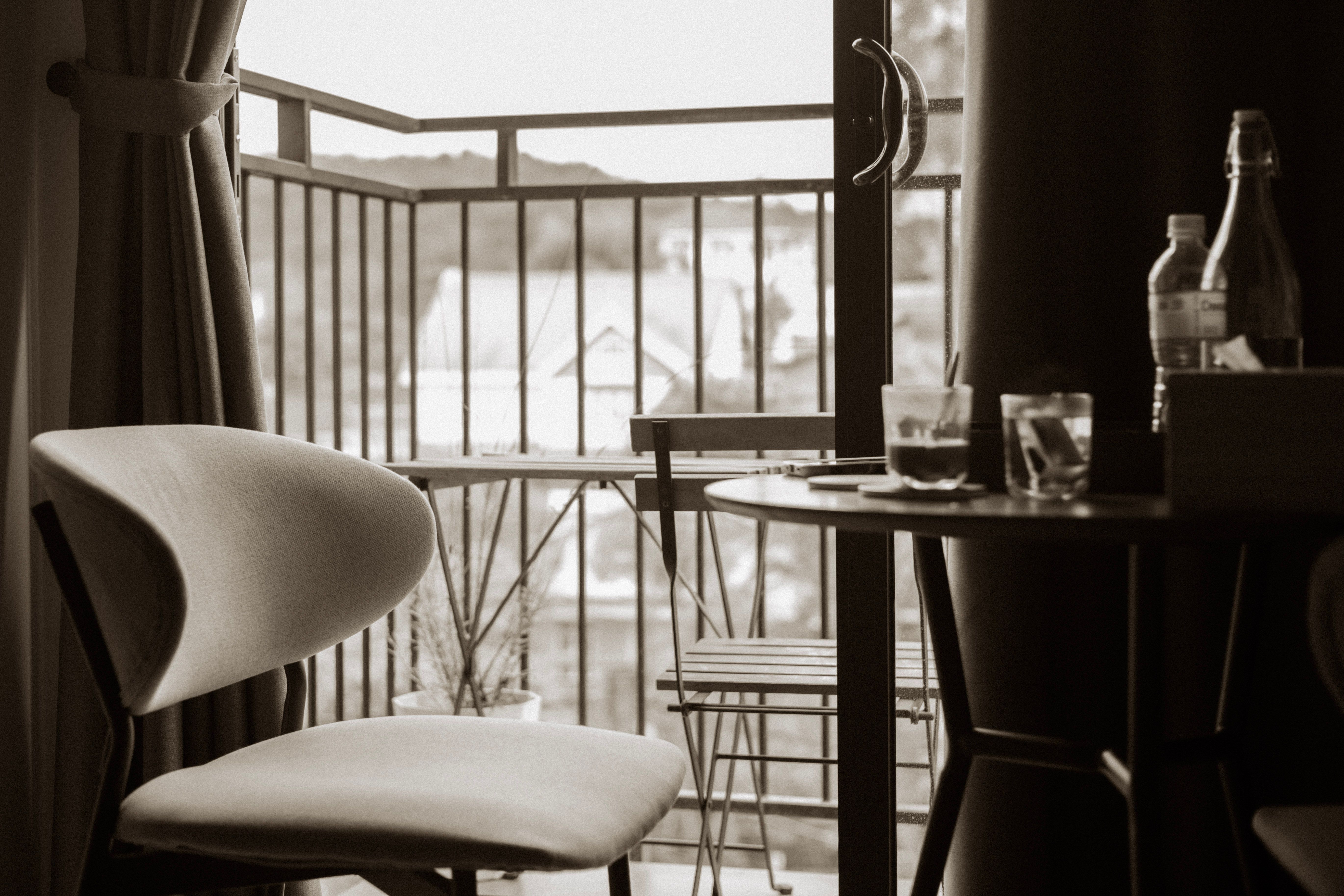 Sepia-toned indoor view of a balcony with chairs, table, and soft curtain lighting.