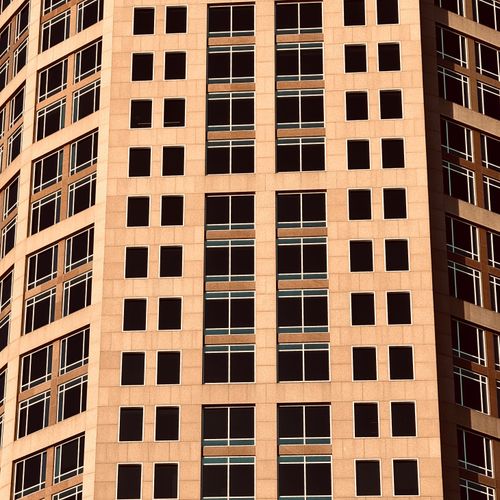 Free Close-up view of a modern skyscraper facade featuring symmetrical geometric windows in warm lighting. Stock Photo