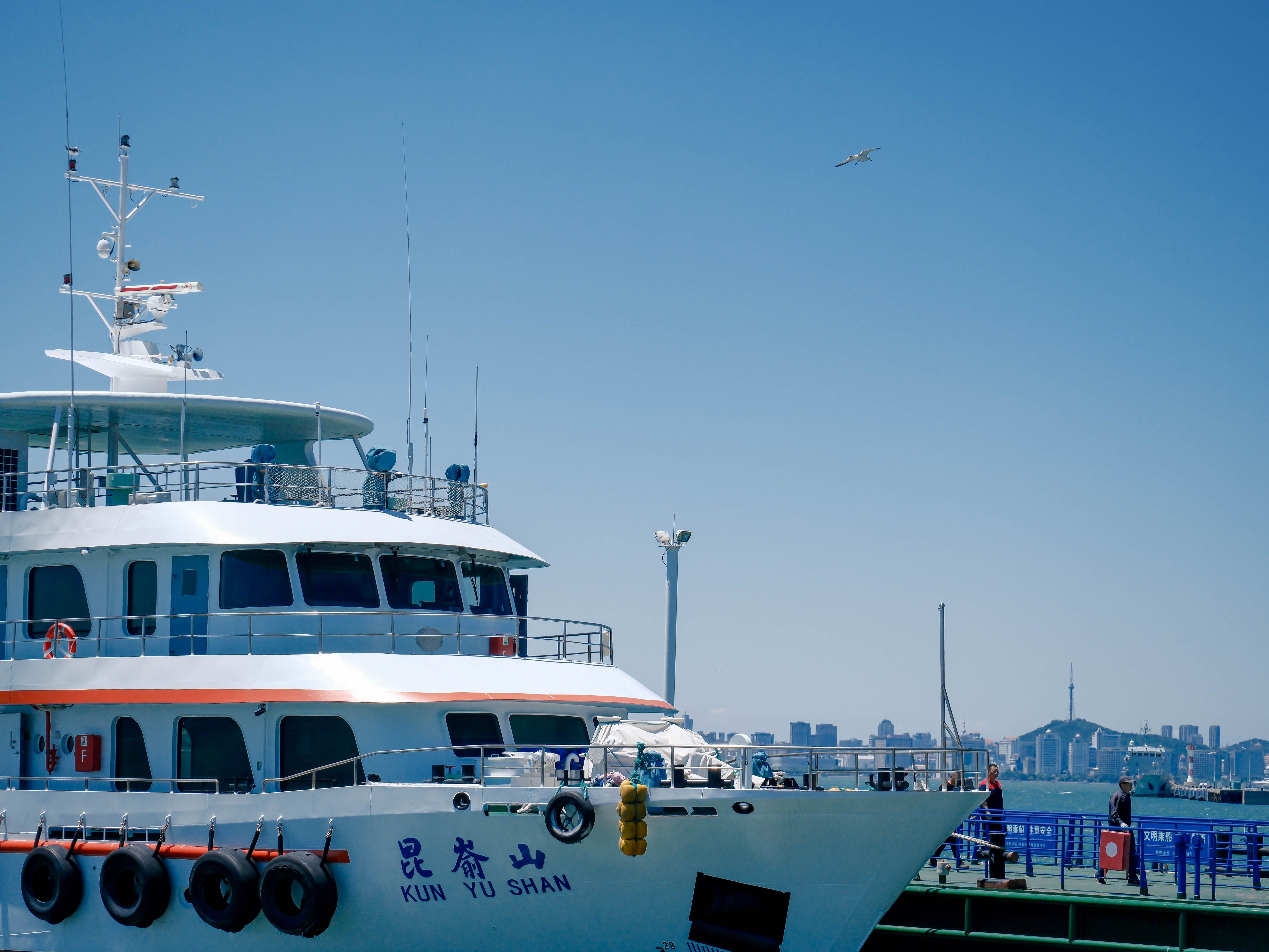 A ferry named 'Kun Yu Shan' docked at a bustling city marina under a clear blue sky.