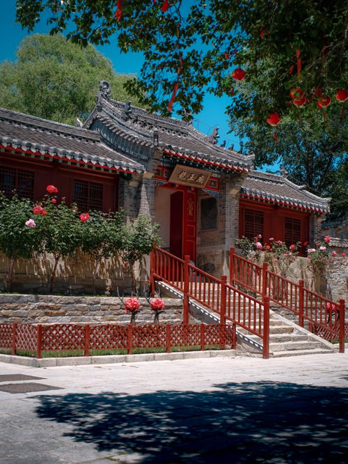 Free A vibrant Chinese building surrounded by lush greenery and blooming flowers. Stock Photo