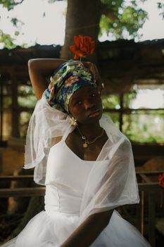 Beautiful portrait of a woman in traditional Nigerian attire with floral headscarf in a natural setting.