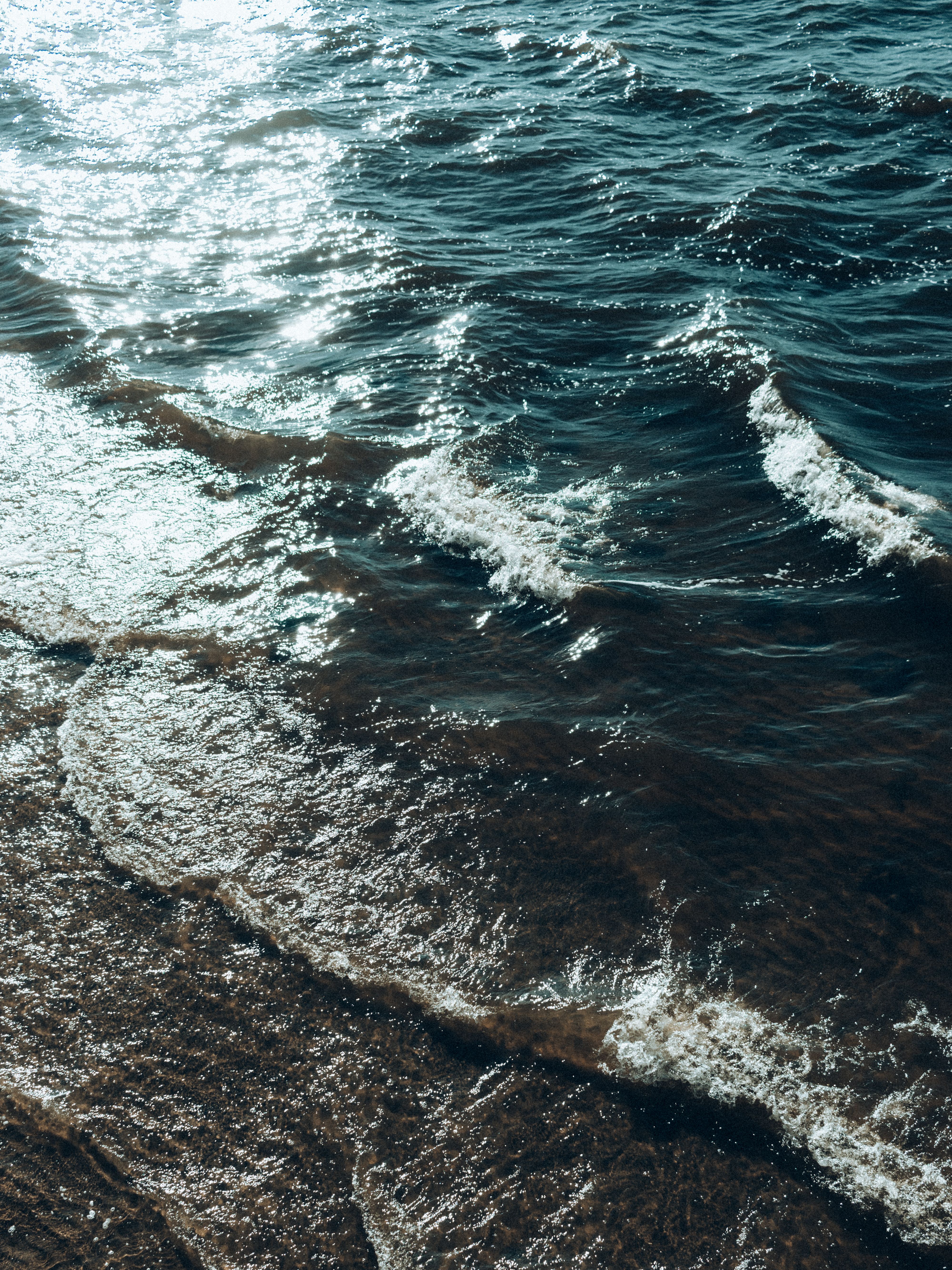 Serene coastal scene with sunlight reflecting off ocean waves and sandy shore.