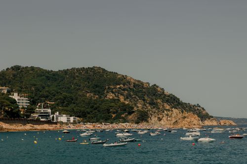 Free Scenic view of boats along the coastline of Tossa de Mar, Spain, with lush hills and turquoise waters. Stock Photo