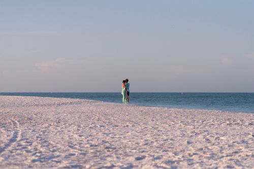 Free A couple enjoying a peaceful walk on a sunlit beach with calm sea and clear sky. Stock Photo
