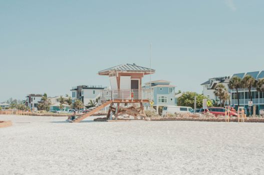 A sunny beach scene featuring a lifeguard hut and beachfront houses under a clear blue sky.