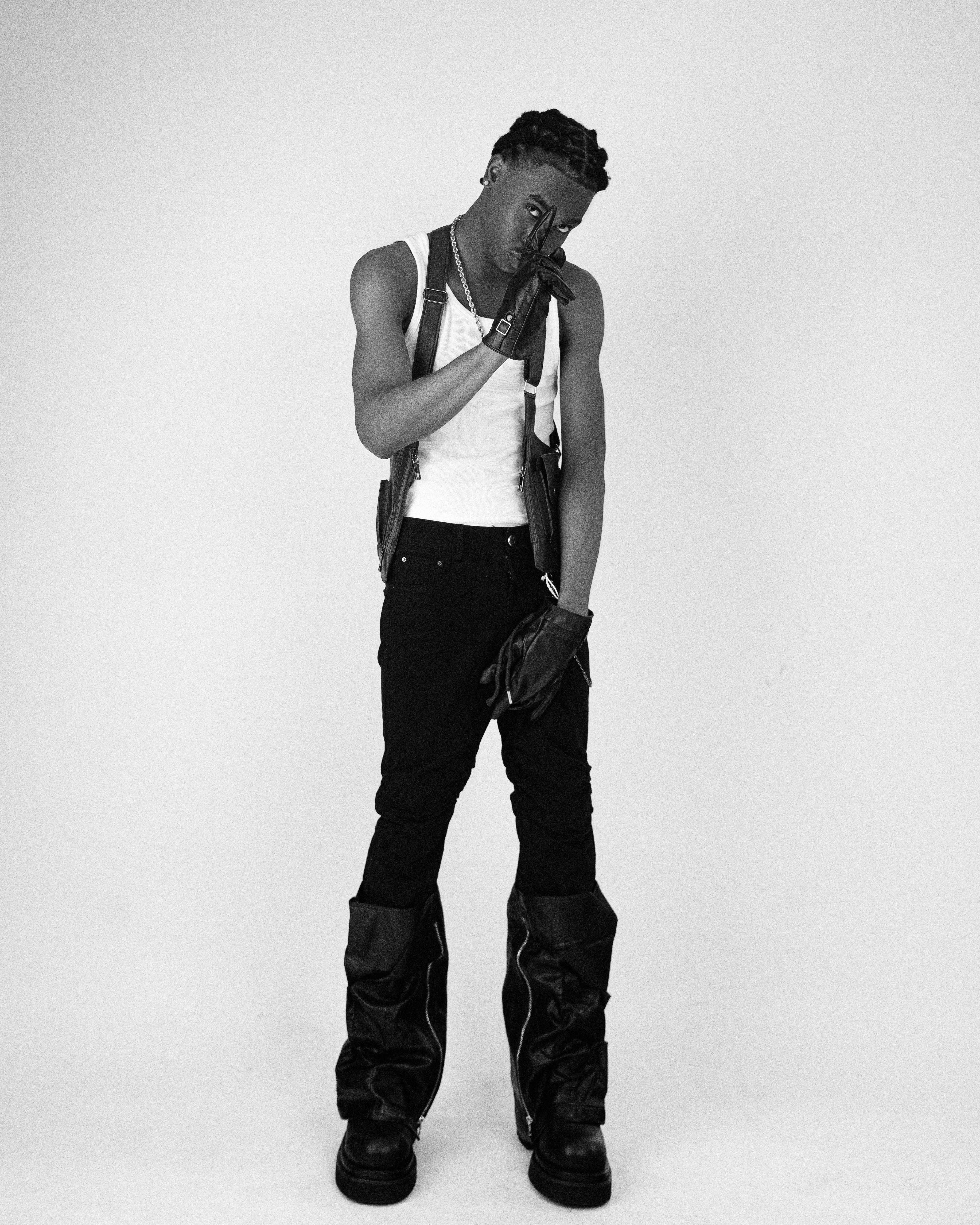 Black and white portrait of a stylish young man in punk fashion with gloves and boots.