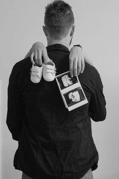 A couple embracing, holding baby shoes and ultrasound images, symbolizing pregnancy announcement.