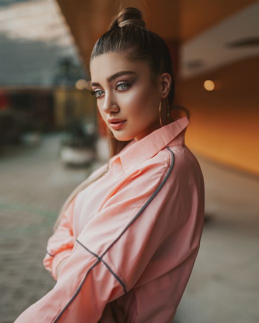 Portrait of a stylish young woman in a pink shirt with a blurred outdoor backdrop, exuding confidence.