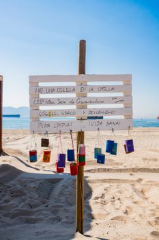 Sign on a sandy beach promoting environmental awareness, featuring colorful recycled containers.