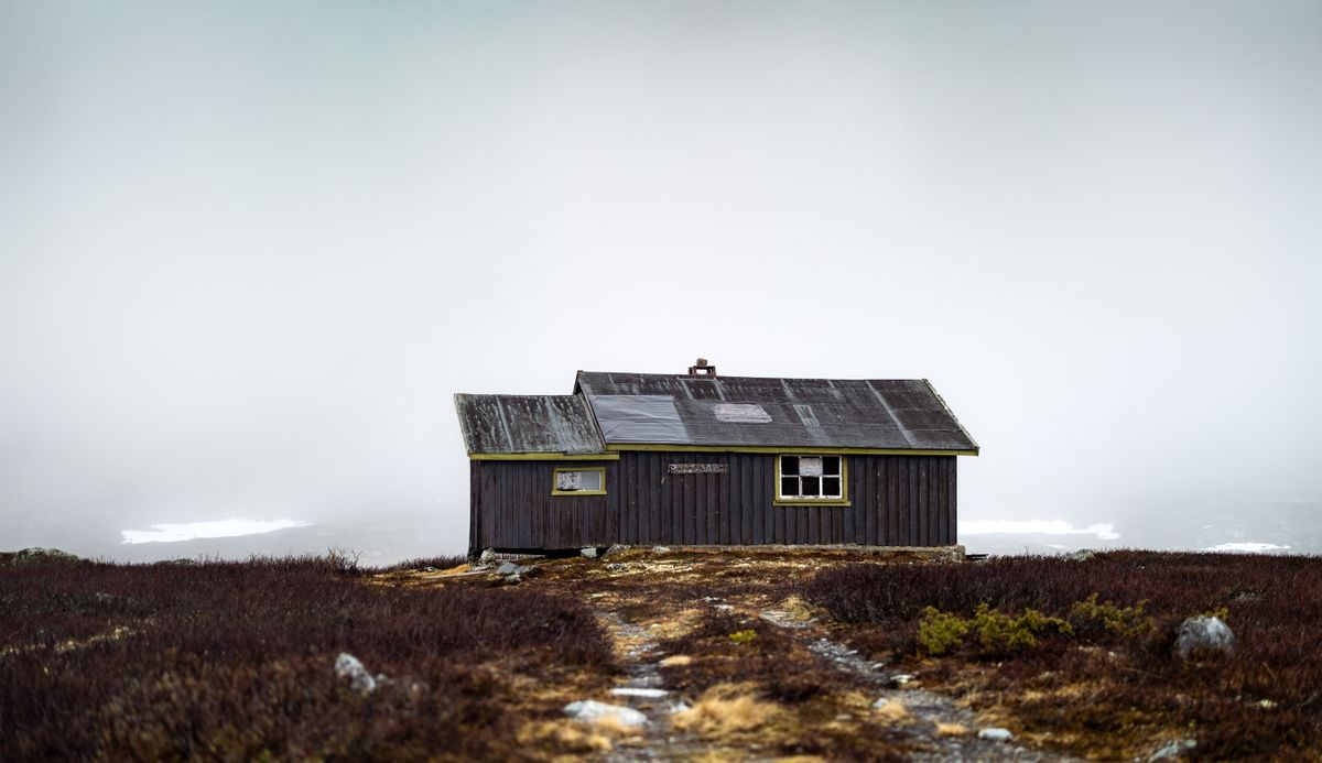 A dark wooden hut alone on a foggy moorland, barely visible in the mist.