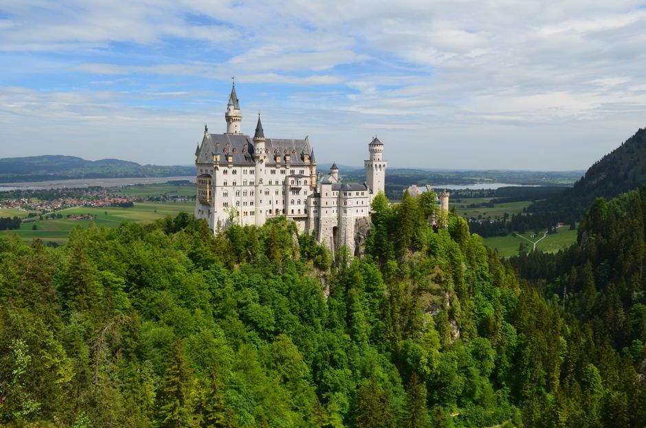 Capture of iconic Neuschwanstein Castle surrounded by vibrant green forest in Bavarian landscape.