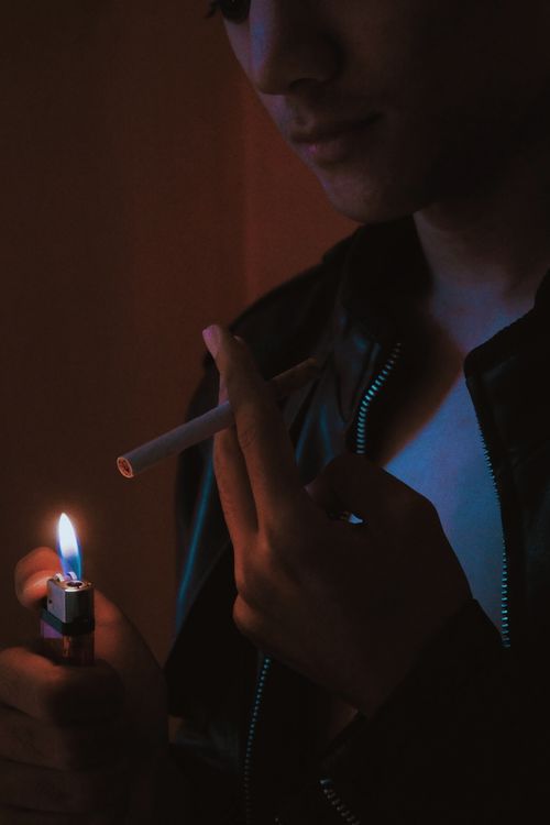 Free Man lighting cigarette with a lighter in a dark, moody setting. Stock Photo