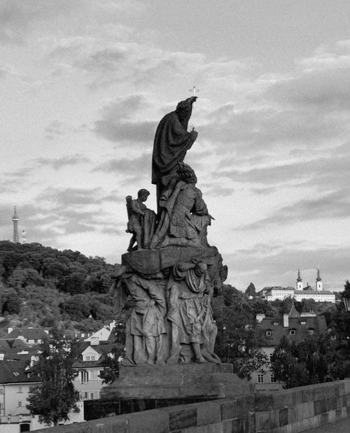 Free Black and white image of a historic statue on Charles Bridge, Prague, against a cloudy sky. Stock Photo