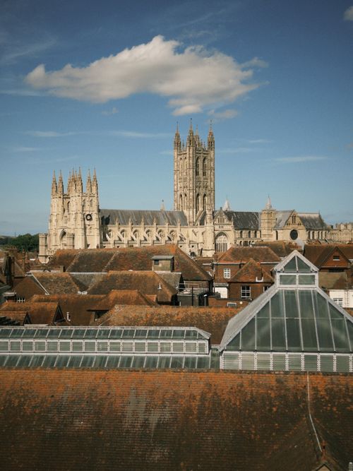 Free An aerial view showcases the majestic Canterbury Cathedral amidst historic rooftops under a clear blue sky. Stock Photo