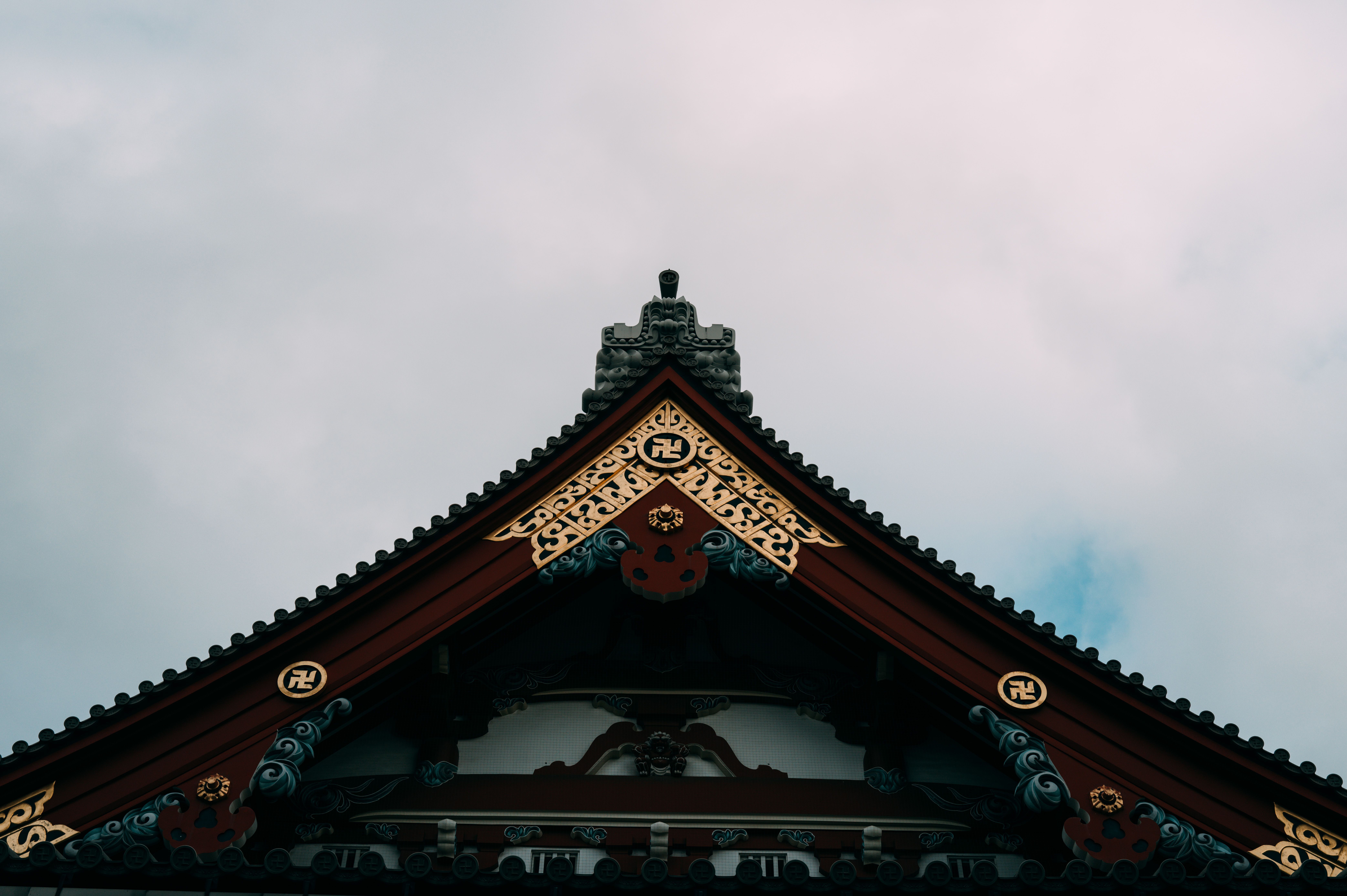 Intricate architectural details of a traditional Japanese temple rooftop under a cloudy sky.