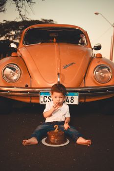 Toddler celebrates second birthday in front of classic orange Volkswagen Beetle.