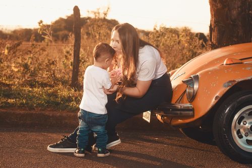 Free A nurturing moment between mother and child by a vintage car during sunset. Stock Photo