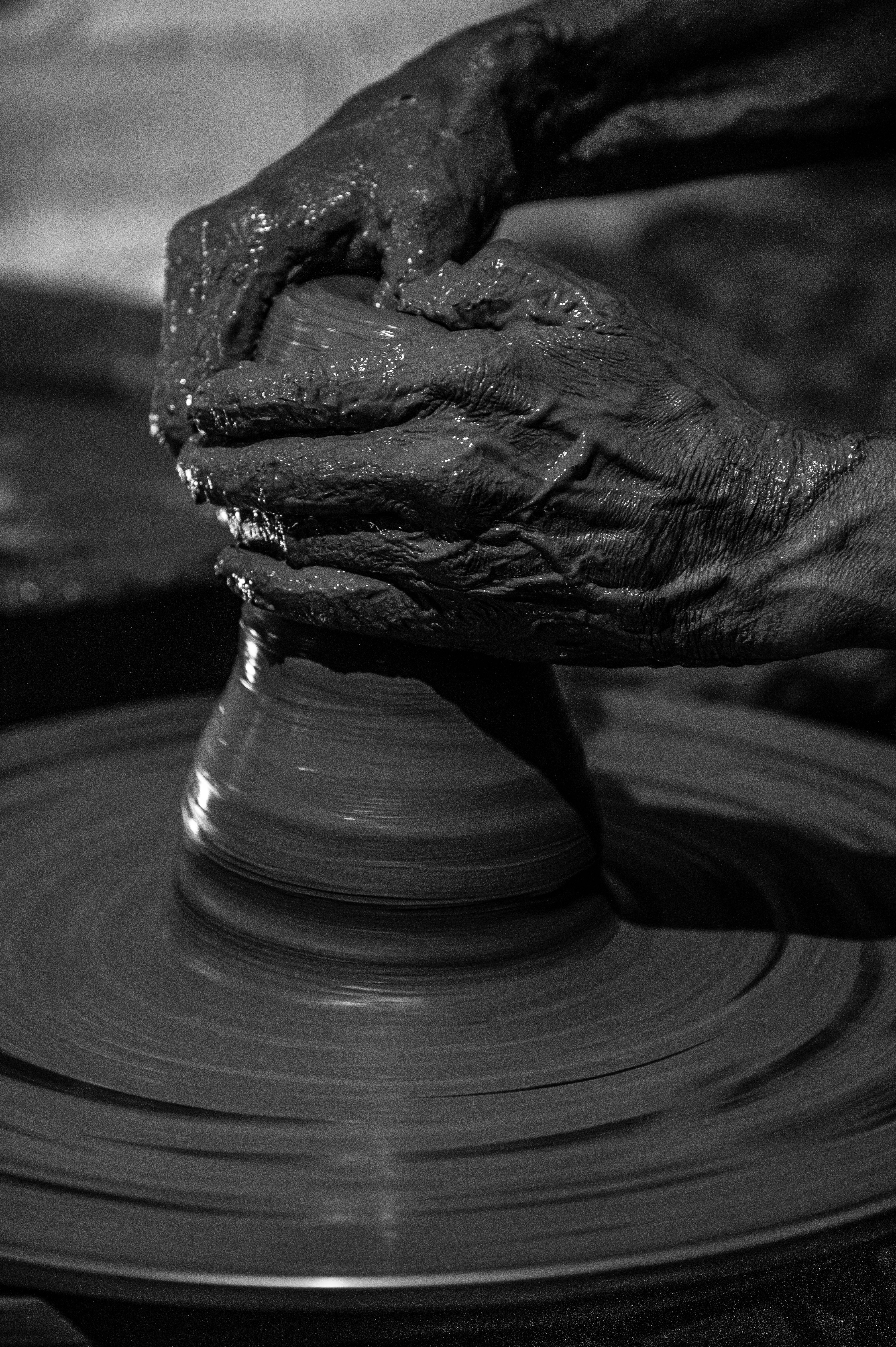 Black and white close-up of skilled hands shaping clay on a pottery wheel.