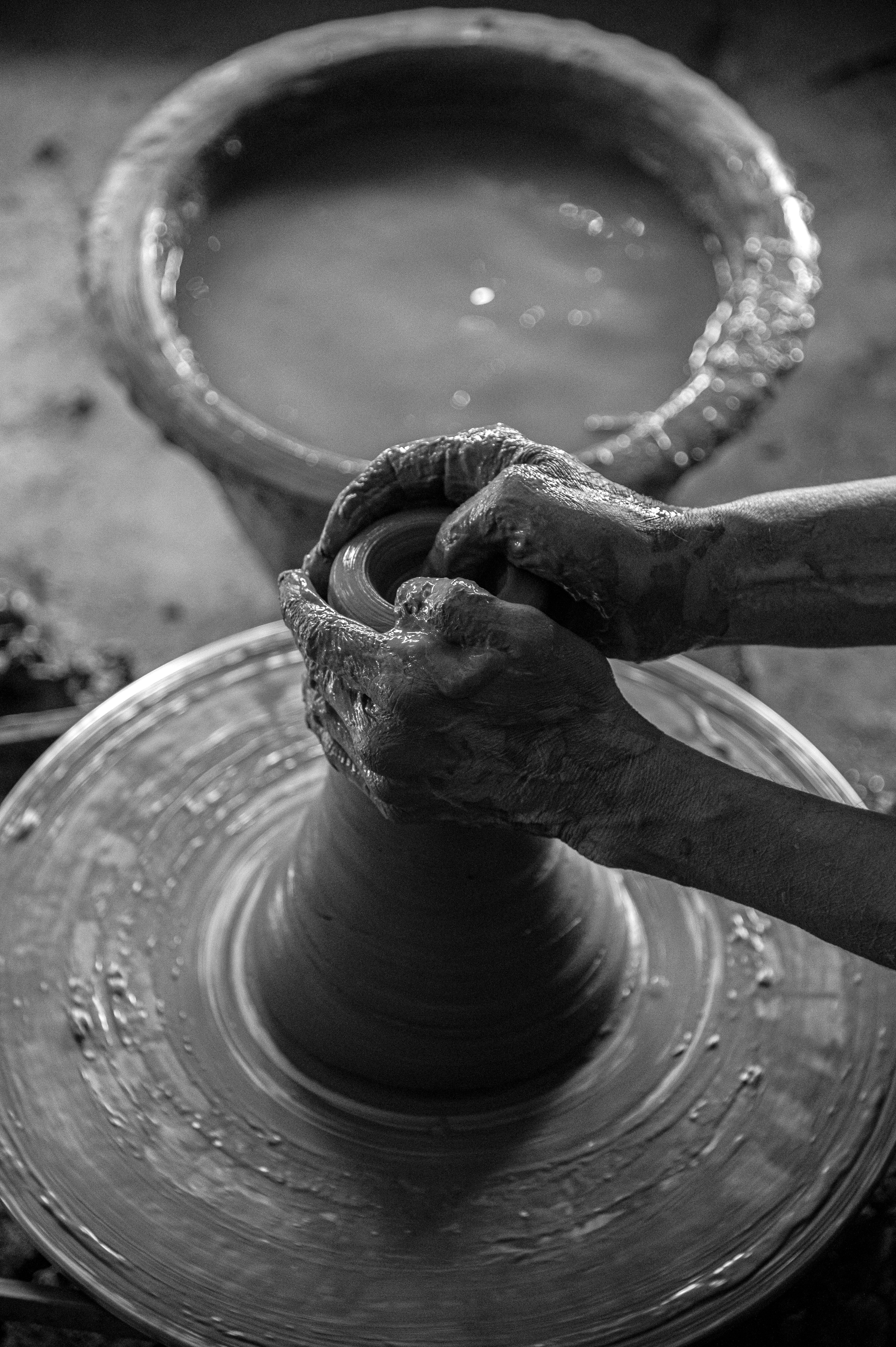 Black and white photo of hands molding clay on a spinning potter's wheel, showcasing artisanal craftsmanship.