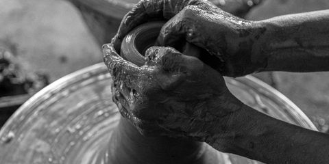 Black and white photo of hands molding clay on a spinning potter's wheel, showcasing artisanal craftsmanship.