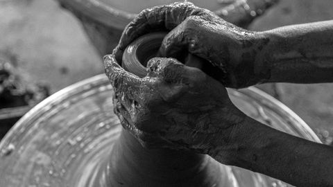 Black and white photo of hands molding clay on a spinning potter's wheel, showcasing artisanal craftsmanship.