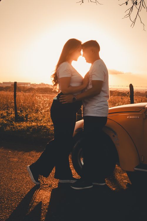 Free A couple embraces near a vintage car at sunset, highlighting romance and warmth. Stock Photo
