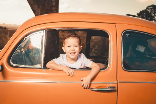Happy child looking out of a vintage orange car in a sunny outdoor setting.