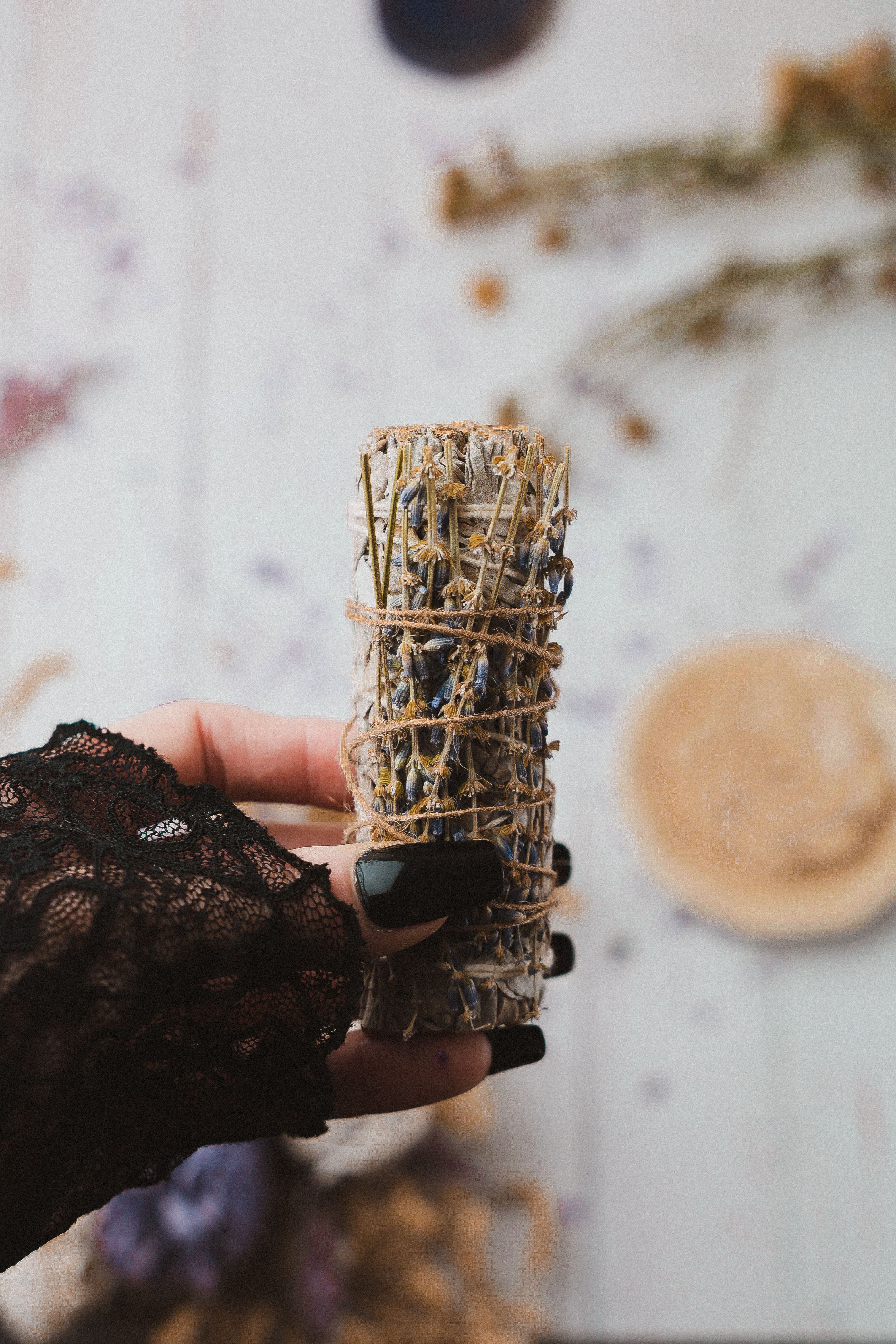 A hand adorned in black lace holds a sage smudge stick, creating a mystical atmosphere.