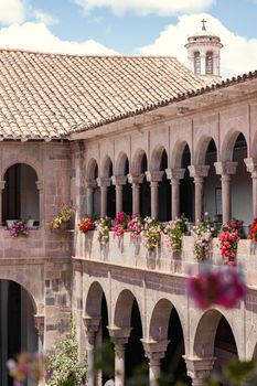 Sunlit courtyard with stone arches and vibrant flowers in Cusco, highlighting Peruvian architecture.
