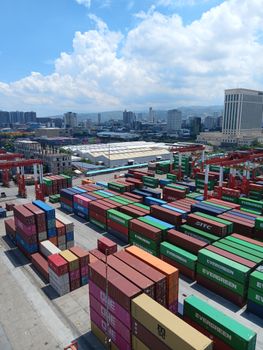 Aerial view of vibrant shipping containers stacked at a busy Manila port under a bright sky.