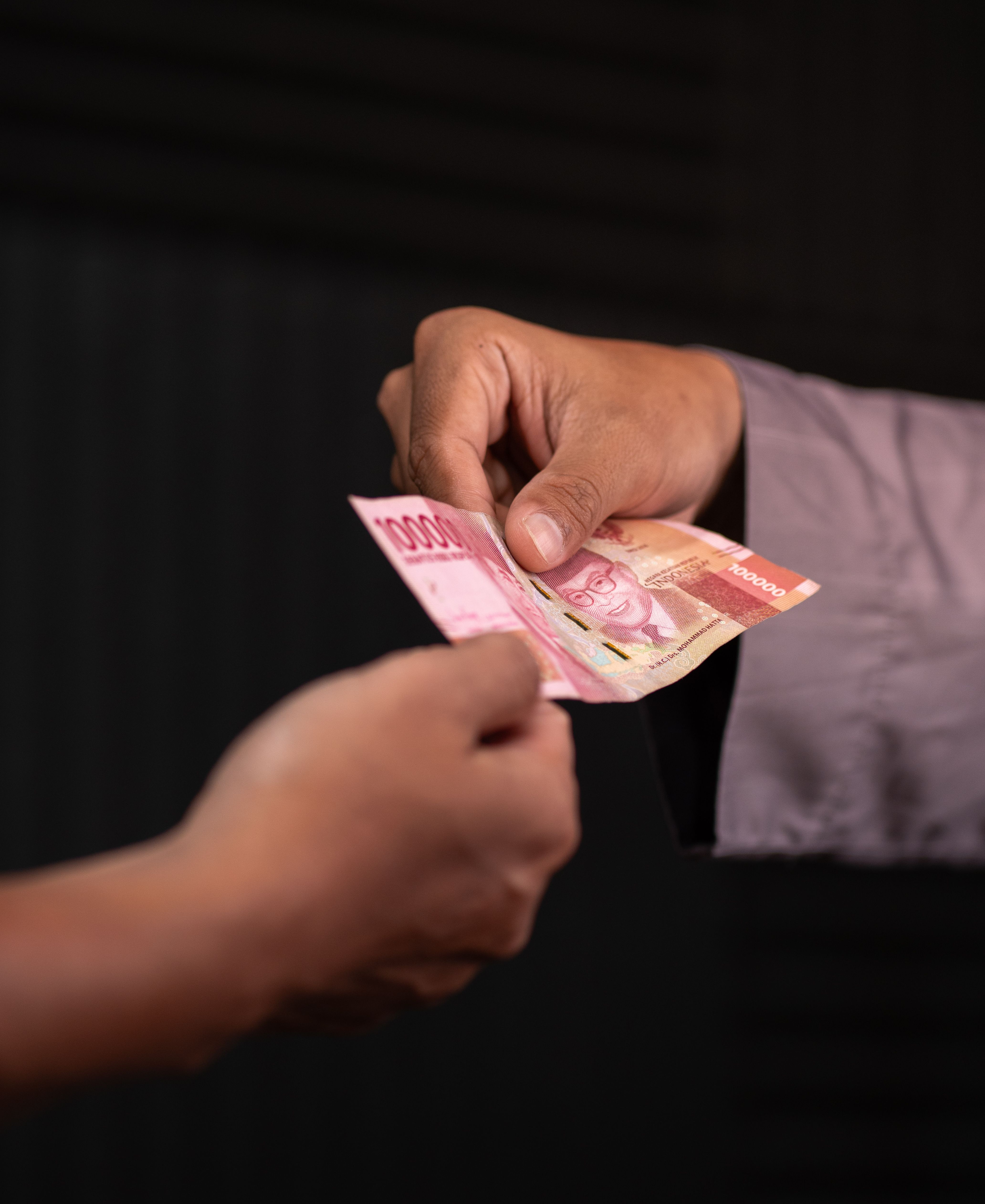 Close-up of a person giving 10000 rupiah notes, symbolizing donation or charity.
