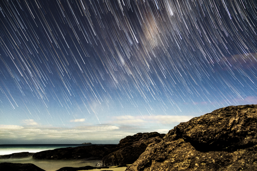 Long exposure capturing star trails over a rocky coastline in Hawks Nest, Australia.