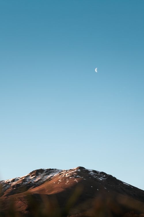 Free A peaceful winter scene in Anhaux, France, featuring a snow-capped mountain and crescent moon. Stock Photo