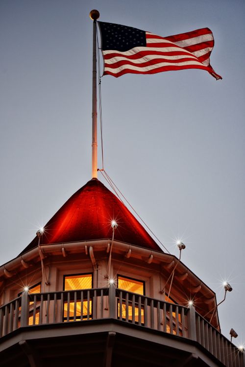 Free American flag waves atop Hotel Del Coronado at dusk, showcasing patriotic spirit. Stock Photo