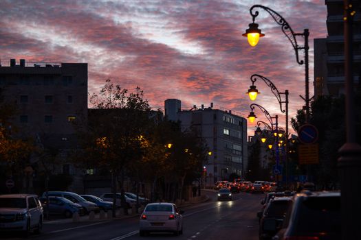 Captivating street view with vibrant sunset sky and illuminated streetlights, featuring silhouetted buildings.