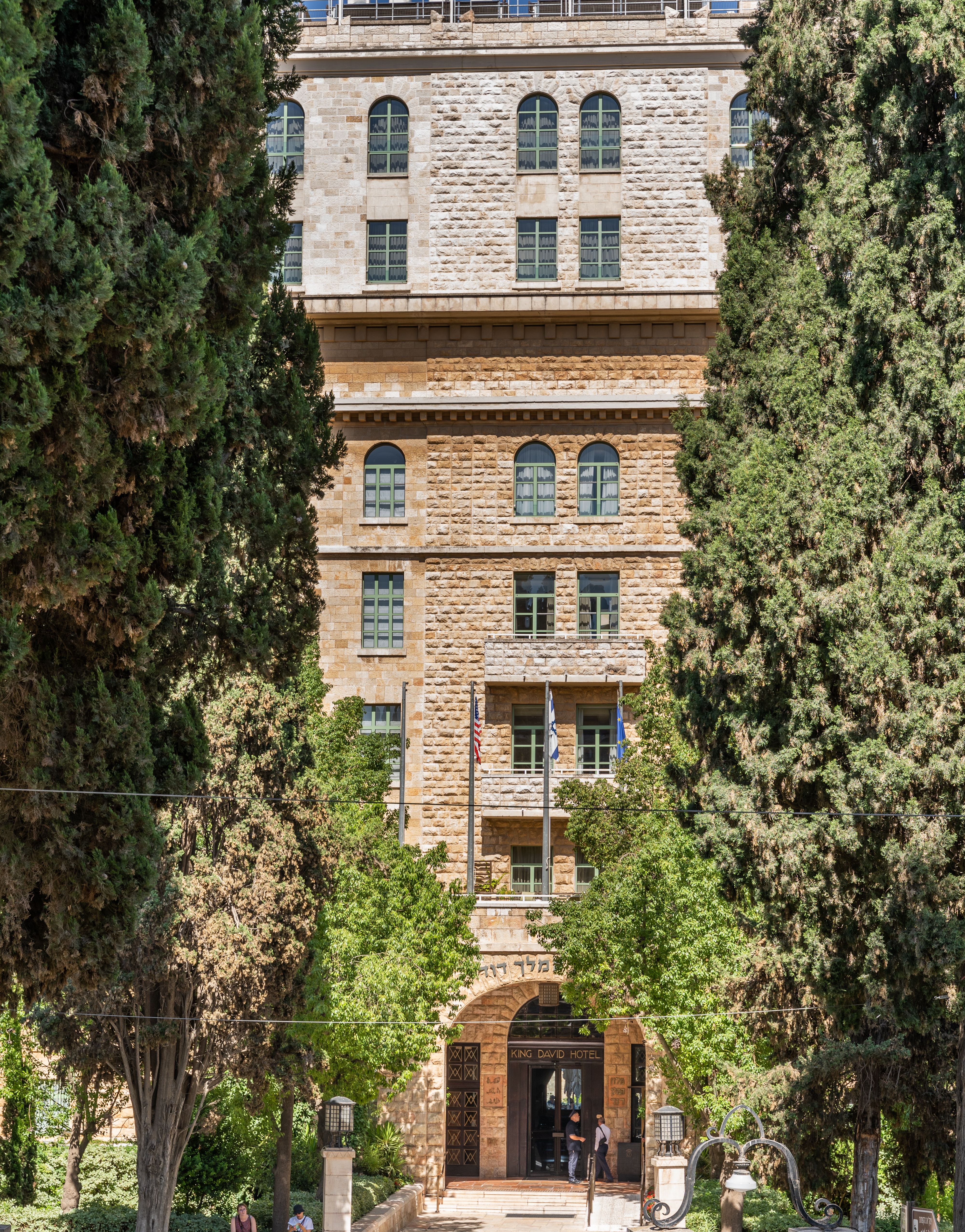 Elegant brick hotel entrance surrounded by lush greenery and flags.