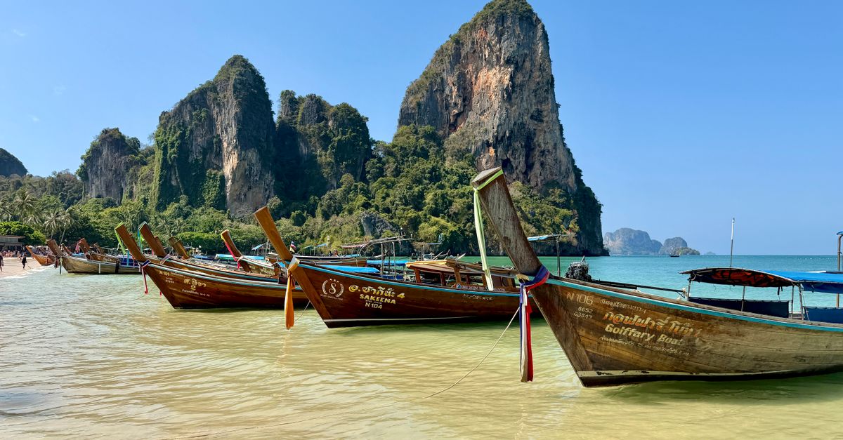 Wooden longtail boats pulled up on the beach at Railay, with limestone cliffs behind.