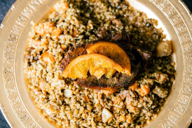 Bulgur pilaf with tender meat and orange garnish served on a decorative plate.