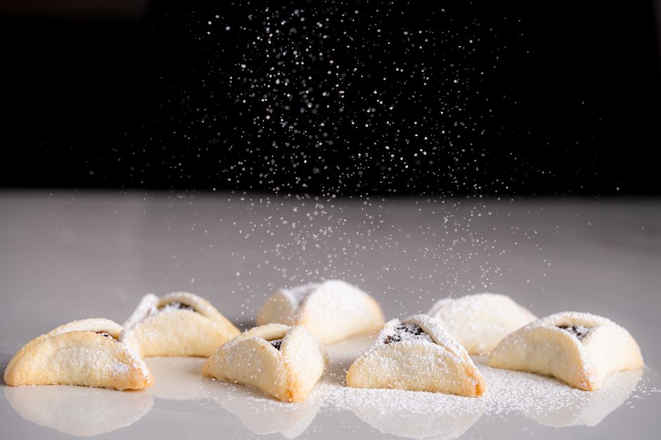 A close-up of freshly baked hamantaschen cookies sprinkled with powdered sugar.