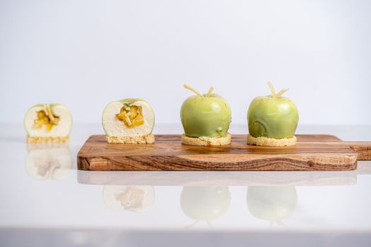 Three green apple mousse desserts elegantly placed on a wooden board, showcasing artistic presentation and delectable design.
