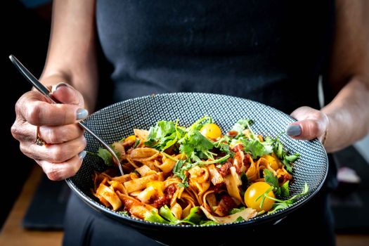 Close-up of woman holding a bowl of fresh pasta garnished with cilantro and cherry tomatoes.