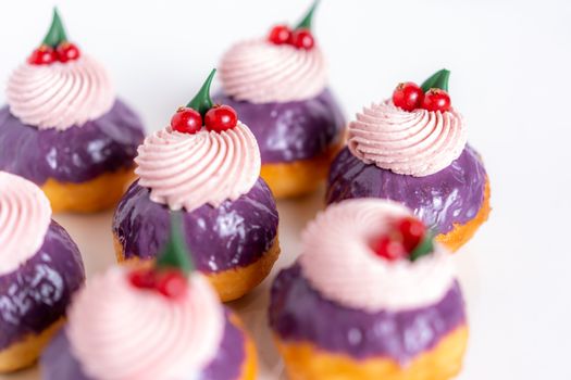 Close-up of colorful purple frosted cupcakes topped with whipped cream and berries on a white background.