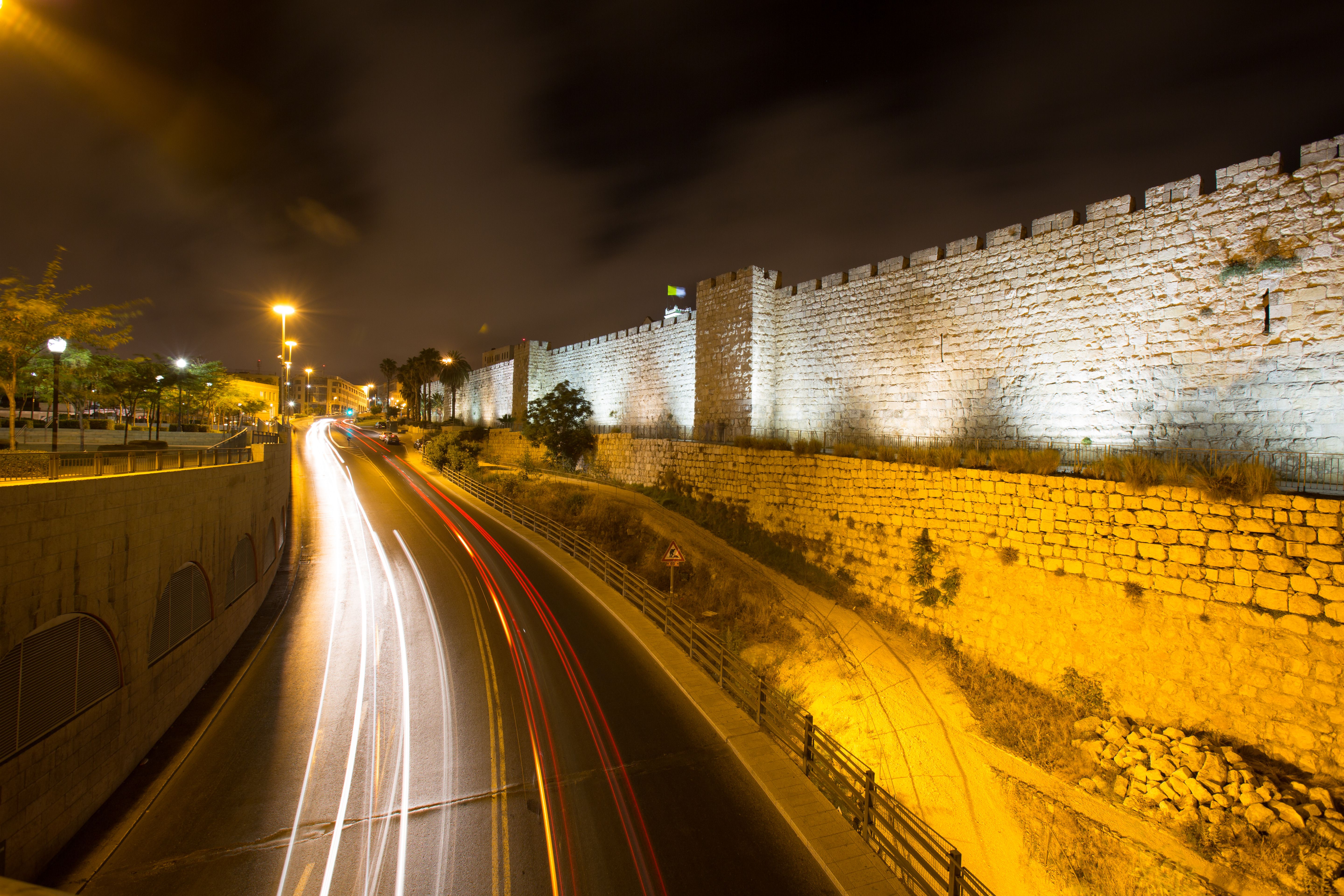 Nighttime photography of a historic stone wall with light trails from passing cars.